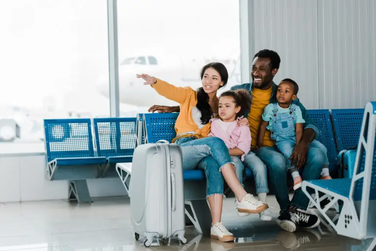 smiling family with baggage and kids sitting in JFK airport while mother pointing with finger away